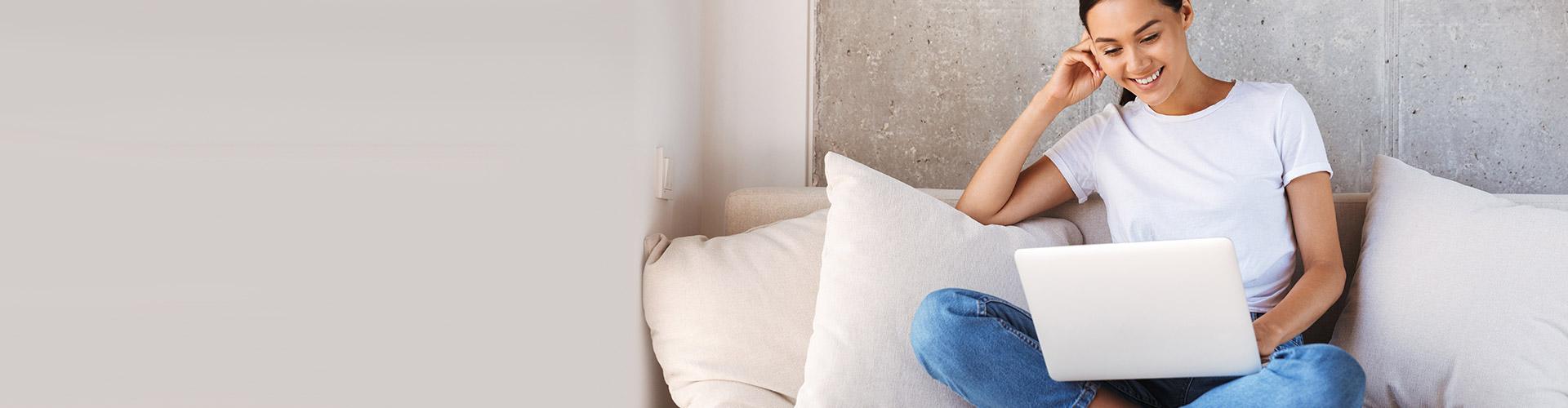 Préstamos - Mujer joven sonriendo con su portátil en el sofá de su casa