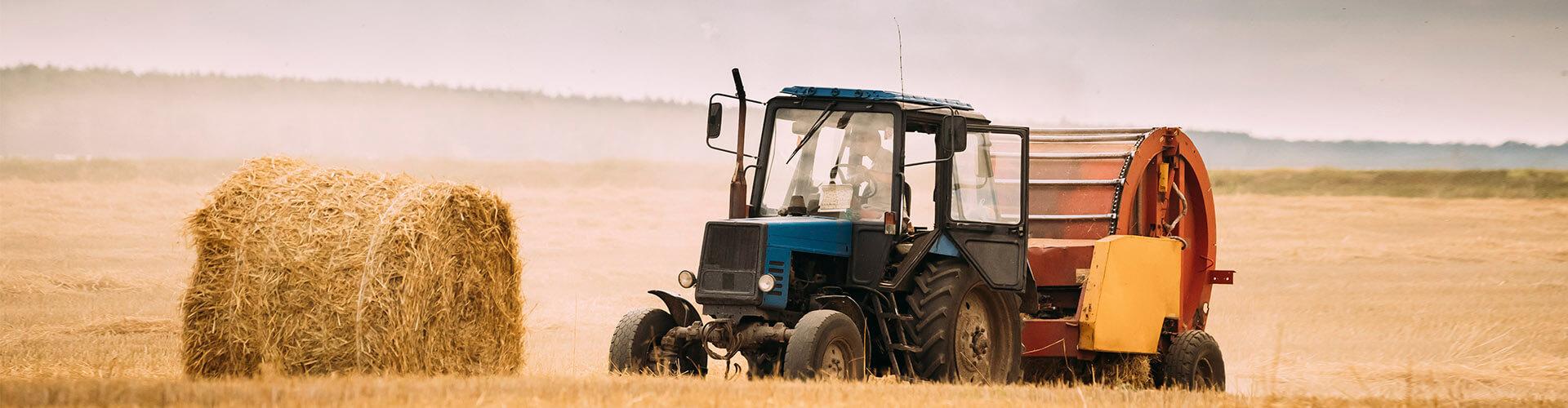 Seguros Agrarios - Tractor azul en el campo recogiendo paja para dar de comer al ganado