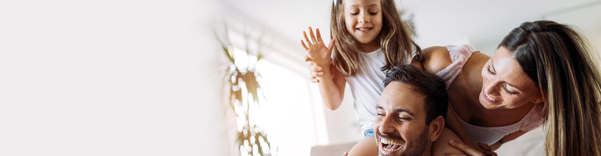 Más seguros para particulares - Familia joven jugando con su hija sonriendo y pasando un buen rato en el salón de su casa