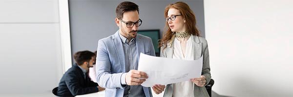 Seguro de Credito - Reunion de negocios entre una mujer con traje gris y un hombre de traje azul mientras estan leyendo unos papeles en una sala de reuniones Seguro de Credito - Reunion de negocios entre una mujer con traje gris y un hombre de traje azul mientras estan leyendo unos papeles en una sala de reuniones