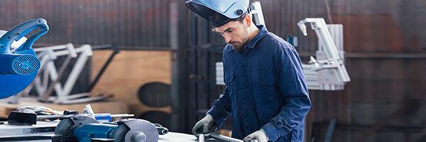 Seguro Multirriesgo Industrial - Hombre con casco y mono azul soldando metal en un taller Seguro Multirriesgo Industrial - Hombre con casco y mono azul soldando metal en un taller