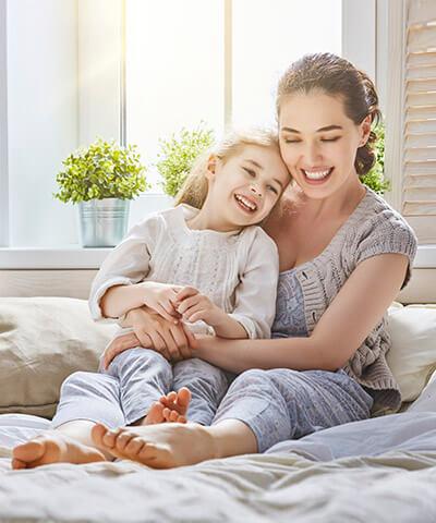 Seguro de Vida - Madre e hija jugando y sonriendo encima de la cama en la habitación de su casa